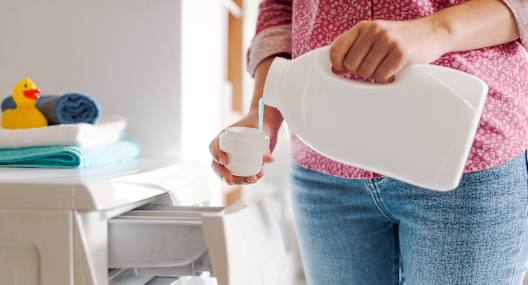 A woman is pouring laundry detergent into a washing machine.
