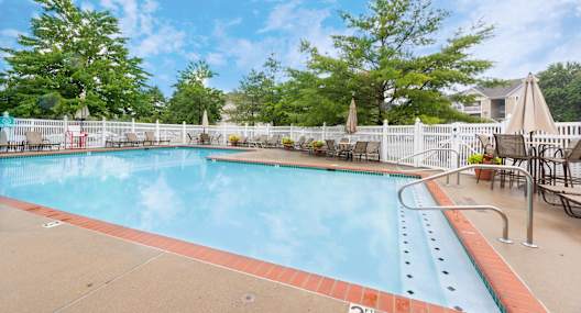 A large outdoor swimming pool surrounded by a white fence and trees.