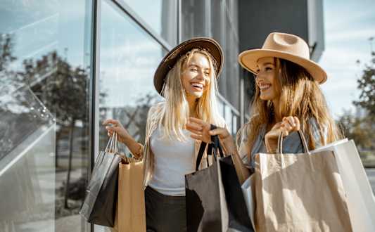 A woman in a black leather jacket holding shopping bags and a coffee cup.