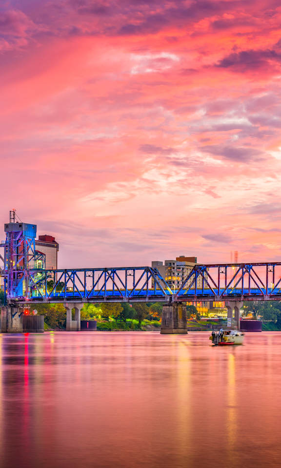A city skyline at dusk with a bridge crossing a river.