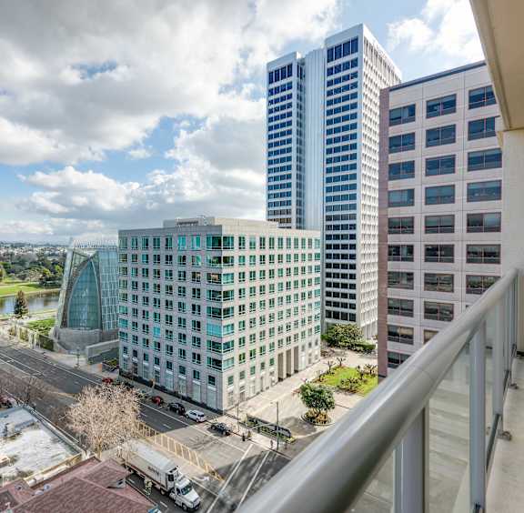 A cityscape with a mix of modern and older buildings, a clear sky, and a parking lot in the foreground at The Grand Apartments, Oakland, CA, 94612