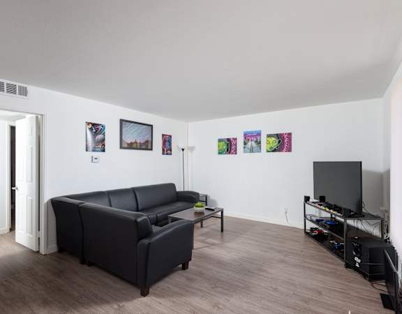 A black leather couch sits in a living room with a television and a wall of pictures.