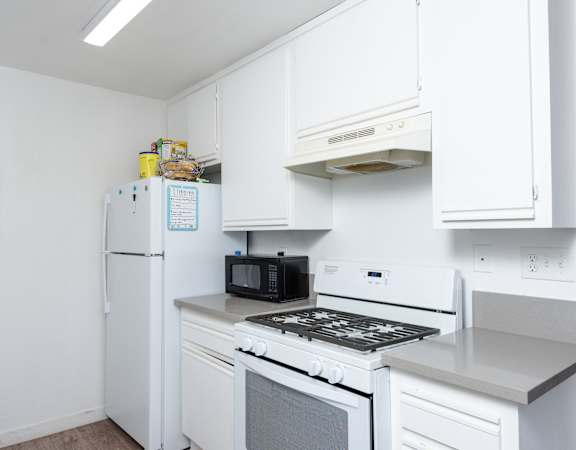 A white kitchen with a fridge, microwave, oven and stove.