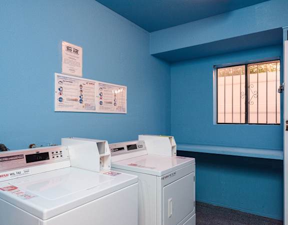 Two white washing machines in a room with blue walls.