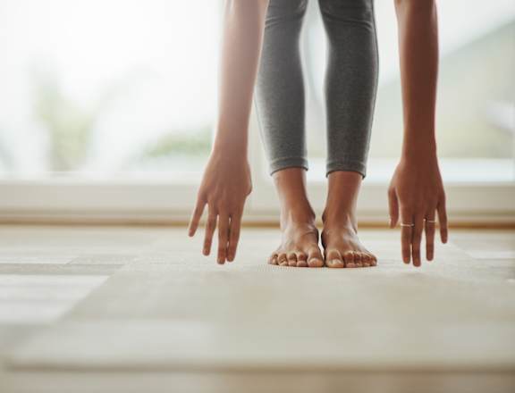 A person is standing on a mat with their hands on the floor.