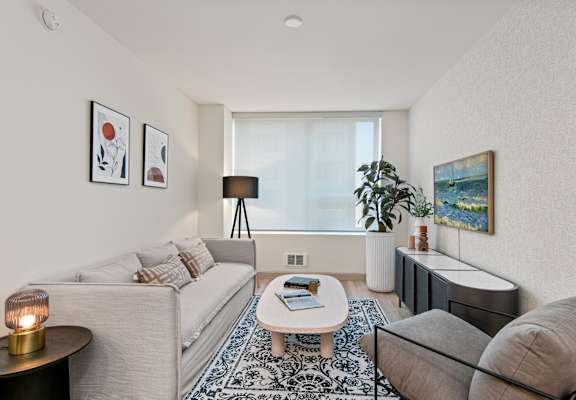 A living room with a grey couch, a white coffee table, and a large window.