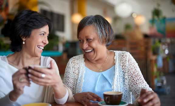 Two women laughing and having coffee together.