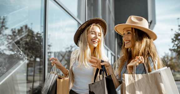 two women holding shopping bags and looking at a store window