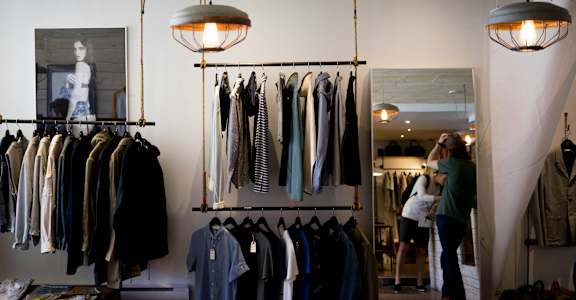 A woman is shopping in a clothing store with a variety of shirts hanging on the racks.