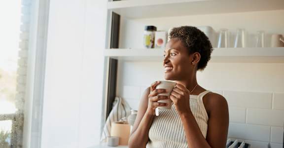 A woman is standing in a kitchen holding a mug.