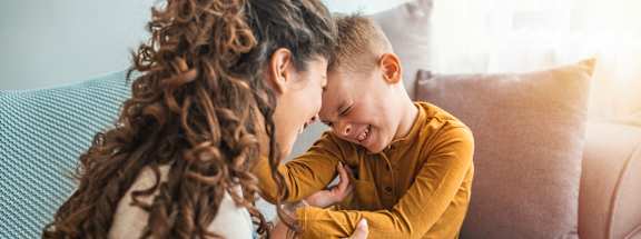 A woman with curly hair is sitting on a couch with a child, both are wearing yellow tops.