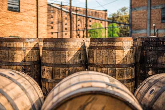 A stack of wooden barrels in front of a brick building.