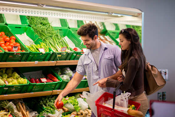 A man and woman shopping for vegetables in a grocery store.