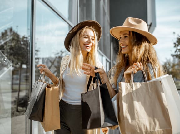 two women holding shopping bags and looking at a store window