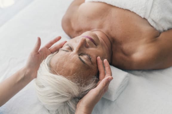 an older woman lying in bed with her eyes closed and her hands on her face