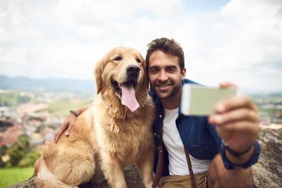 A man is taking a selfie with his golden retriever in front of a scenic view.