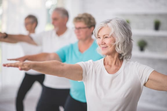 An older woman with her arms out in a yoga class