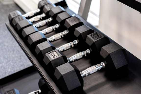 A set of black dumbbells are lined up on a rack.