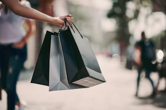 A person is holding three black shopping bags.