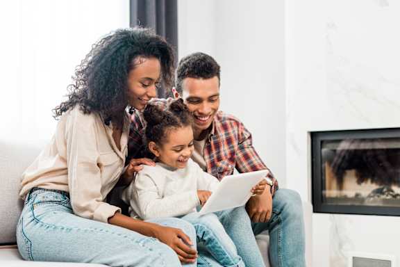 a family sitting on a couch looking at a tablet
