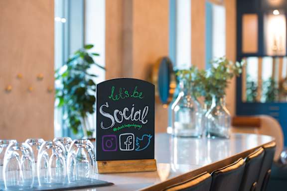 A sign that says "Let's be Social" is on a table with glasses.