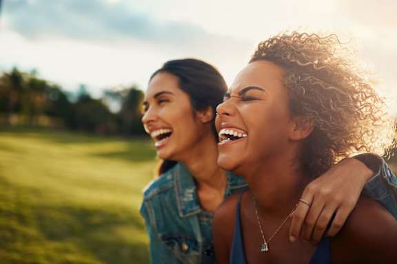 Two women laughing together in a sunny outdoor setting at The Foundry Apartments, Bordon, GU35 9FE