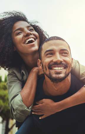 A man is giving a piggyback ride to a woman in a city setting.