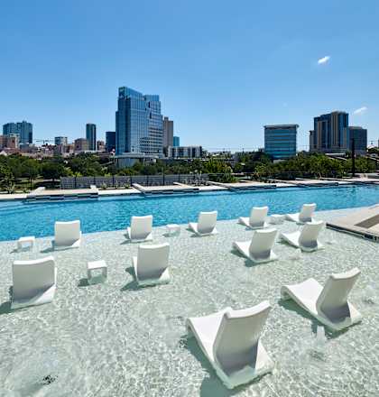 A pool with white chairs and a city skyline in the background.