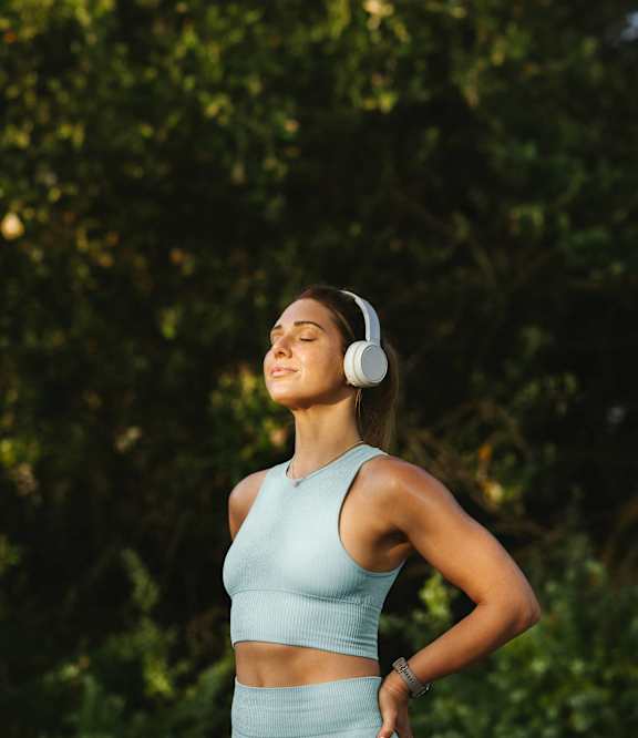 A woman in a blue top and skirt is listening to music with white headphones.