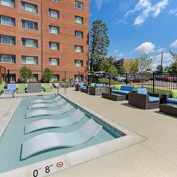 A swimming pool with a depth marker reading 0'8" is in front of a red brick building.