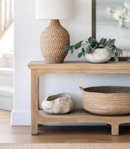 a wooden shelf with a lamp and a table with baskets and a mirror