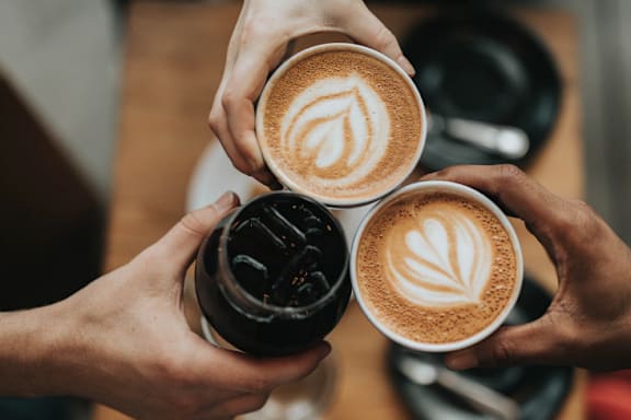 Three hands holding cups of coffee with latte art on top.