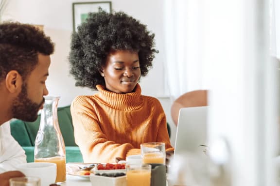 A man and a woman are having breakfast and using a laptop.