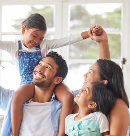 A family of four is sitting on a couch, with two children being held up by their parents.