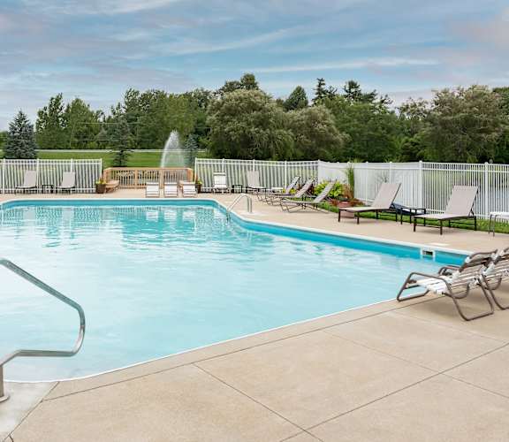 A large swimming pool with a fountain in the middle and lounge chairs around it.