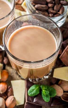 A glass of coffee with hazelnuts and chocolate around it.
