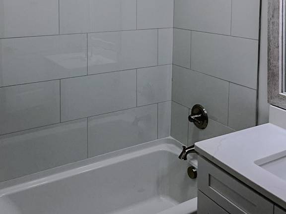 A white tiled shower with a white tub and a white sink.