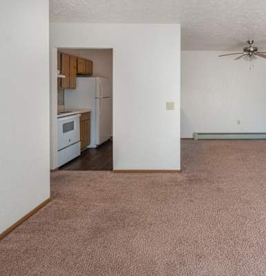 an empty living room with a ceiling fan and a kitchen