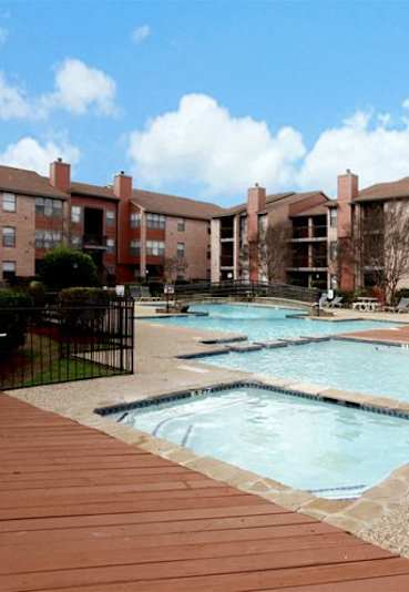 A large outdoor swimming pool surrounded by a black fence and a wooden deck at Brook Meadow Village Apartments , Austin, TX, 78758