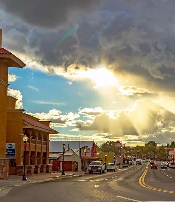 A street scene with cars and buildings under a cloudy sky with sun rays breaking through.