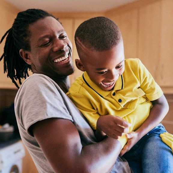 A man with dreadlocks is holding a young boy in his arms.