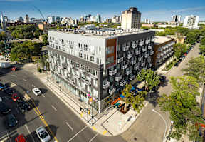 A modern apartment building is situated on a busy street corner with cars parked along the curb.