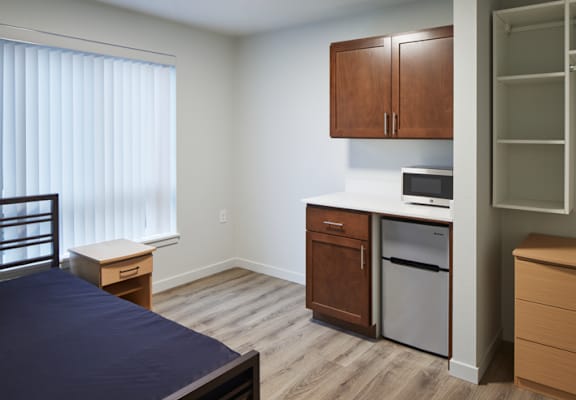 A bedroom with a bed, nightstand, and a small kitchenette.
