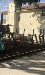 A playground with a green slide and a brown fence.