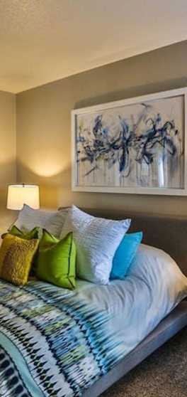 A bedroom with a bed, a side table, and a painting on the wall.