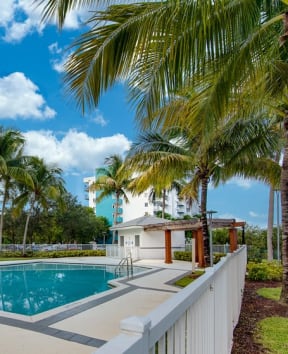 the pool is surrounded by palm trees and a white fence
