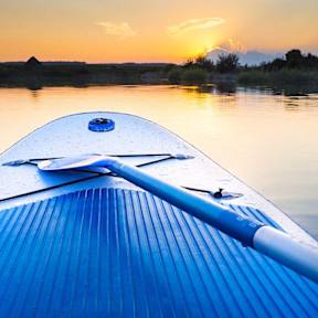 the bow of a blue boat on a river at sunset