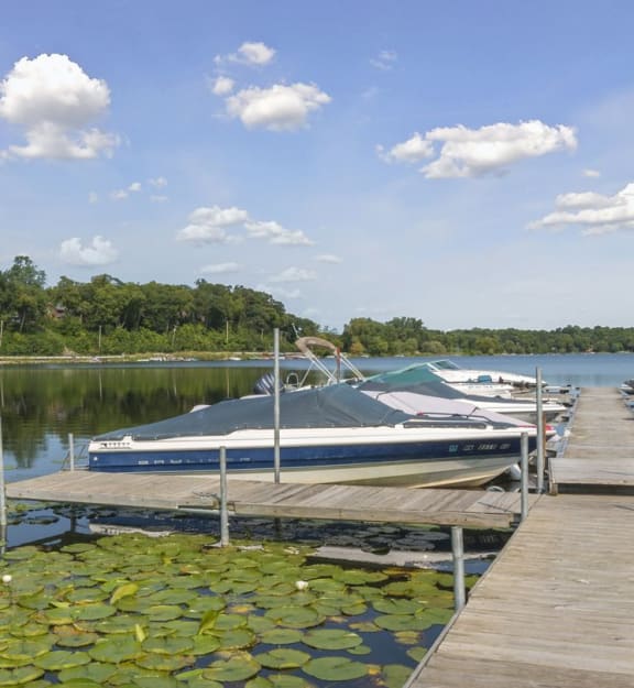 A boat is docked at a pier with lily pads in the foreground. at Medicine Lake Apartments, Minnesota, 55441