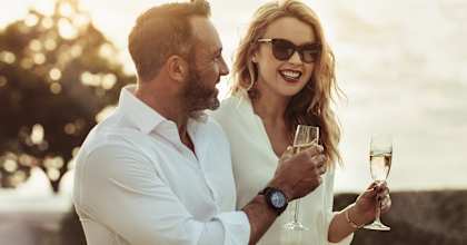 A man and a woman are standing close together, holding wine glasses and smiling.