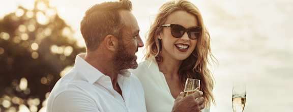 A man and a woman are standing close together, holding wine glasses and smiling.